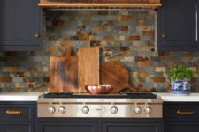 a retro navy kitchen with a wooden hood, gold handles and a gey and brown backsplash of gorgeous tiles