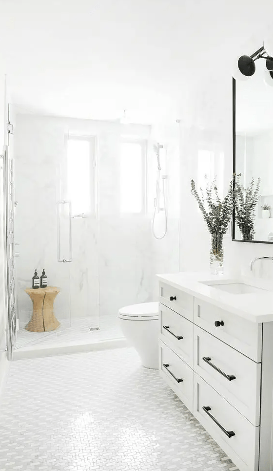 a serene white bathroom with a shaker style vanity, a shower with two windows, a wooden stool in the shower and a mirror