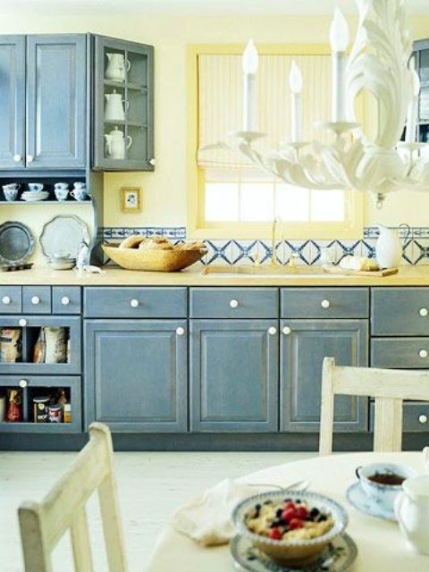 a shabby chic kitchen with shabby blue cabinets, a light yellow backsplash and bright mosaic tiles for a a bold look