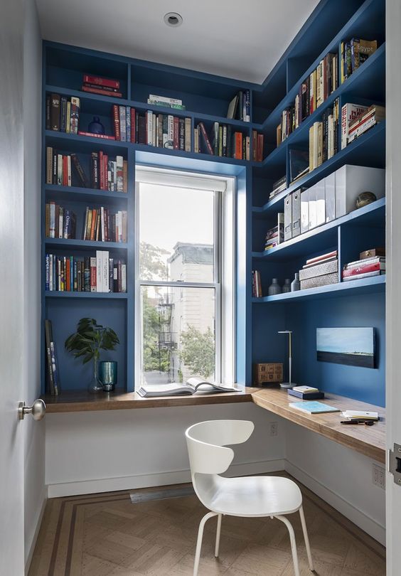 a small and bright home office, all the walls are taken by storage unit, a floating desk and a white chair