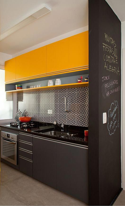 a small black and yellow kitchen with bright upper cabinets, lower grey ones, a mosaic tile backsplash and a chalkboard wall to make notes
