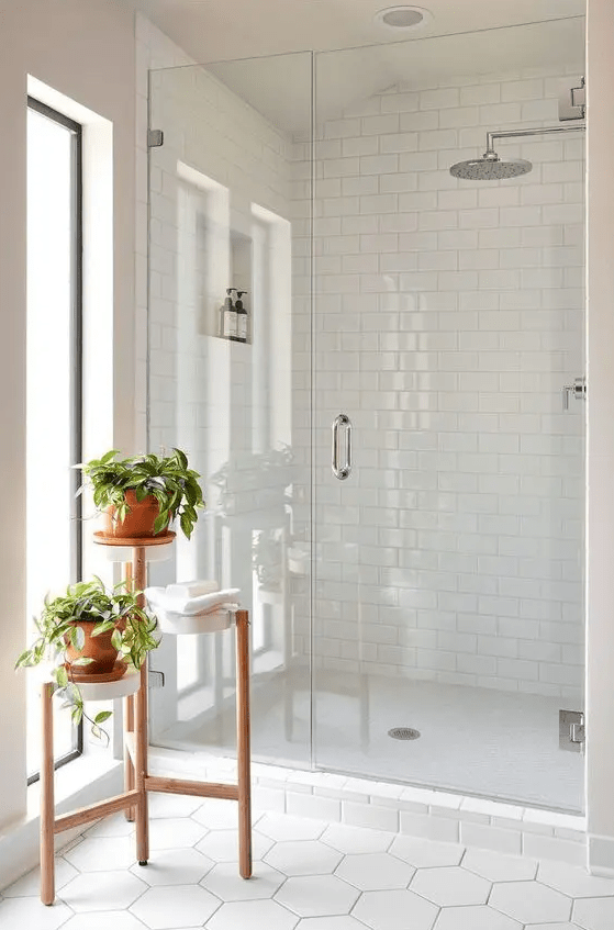 a small white bathroom clad with subway and hexagon tiles, with a tiered plant stand and windows looks awesome