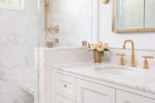 a small white bathroom with a white marble tiles and a countertop, brass and gold fixtures, frames and sconces