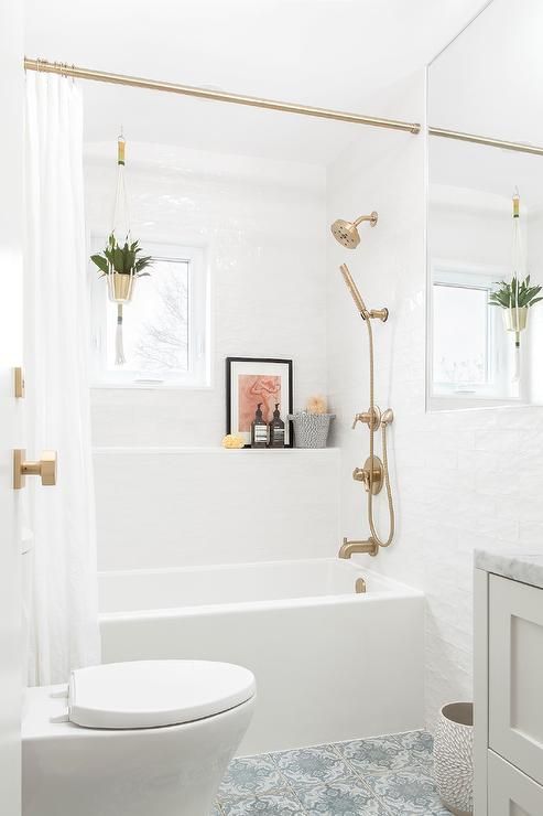 a small white bathroom with brass and gold fixtures and knobs, with a curtain rod and a gold planter to spruce up the space