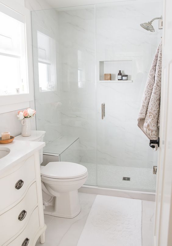 a small white bathroom with marble tiles, a shower space, a white vanity and white appliances is a cool and cozy space