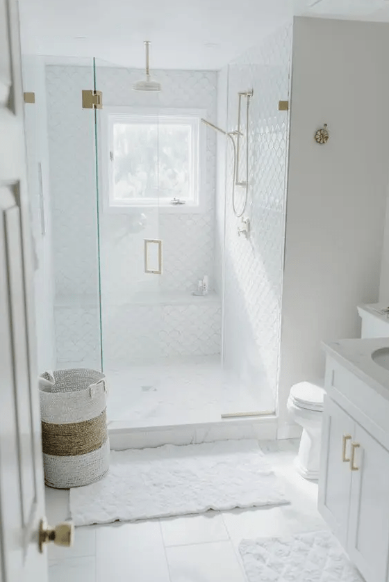 a small white bathroom with scallop tiles and square ones, a shower with a window, white rugs and a basket