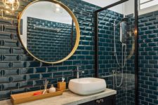 a stylish bathroom clad with teal tiles, with a midnight blue vanity, gold fixtures and a gold frame mirror