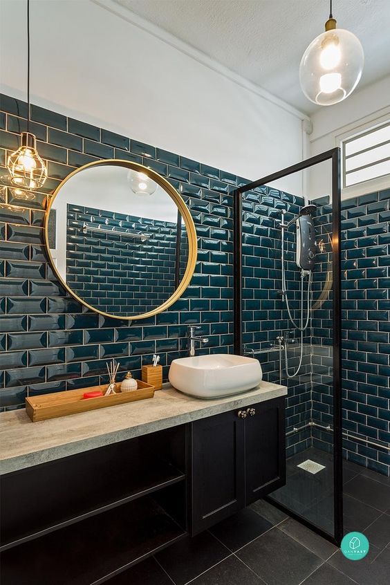 a stylish bathroom clad with teal tiles, with a midnight blue vanity, gold fixtures and a gold frame mirror