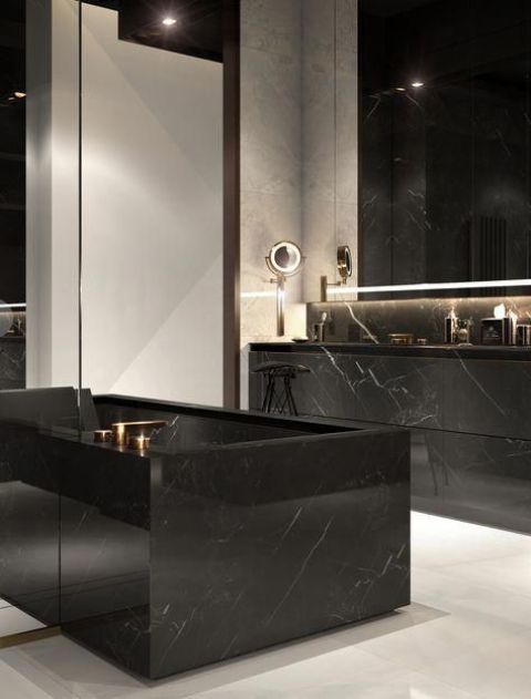 a stylish bathroom with black and white walls, a white floor, a black marble tub and vanity plus lit up mirrors