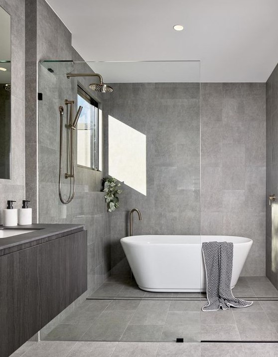 A stylish minimalist bathroom in grey, clad with tiles, with a floating vanity and a free standing bathtub