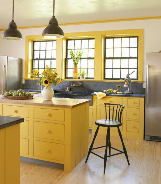 a sunny yellow kitchen with black pendant lamps, a black backsplash and countertop plus black chairs for a new take on traditional decor