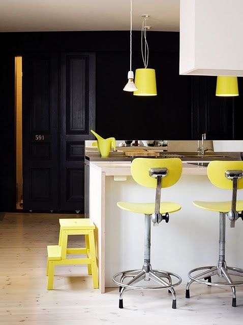 a super bold modern kitchen done with a white kitchen island, hood, black cabinetry and lemon yellow items