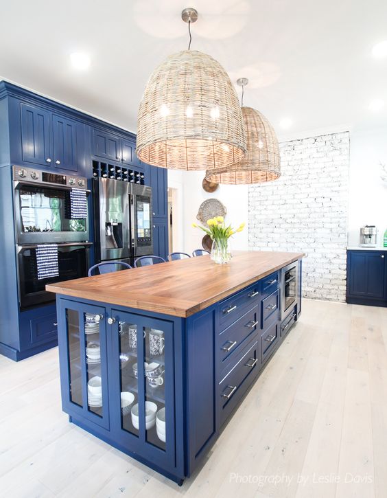 a super bright blue kitchen with a rich stained wooden countertop and wicker lamps over the island