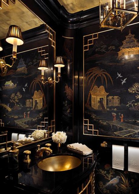a super refined and chic black and gold bathroom with an exquisite artwork, chic lamps and chandeliers, a gold sink and fixtures