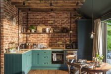 a teal kitchen with a brick wall, a wooden beam installation over the table and a cozy wooden dining set