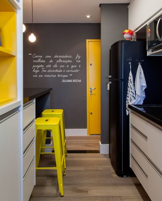 a very small black, white and yellow kitchen with a black fridge and walls, black countertops and touches of various yellow shades