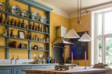 a vintage kitchen done in buttercream and with blue cabinets and open shelving, with vintage pendant lamps and a rustic dining set