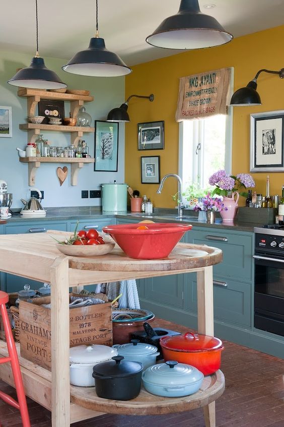 a vintage kitchen with blue cabinets, a mustard and a light blue wall, a wooden kitchen island and black pendant lamps
