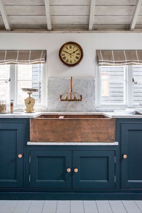 A vintage navy kitchen with a built in copper hammered sink and a matching faucet to make up a bold look