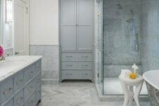 a welcoming grey bathroom done with various tiles, an oversized vanity and a wardrobe plus a metal clad tub