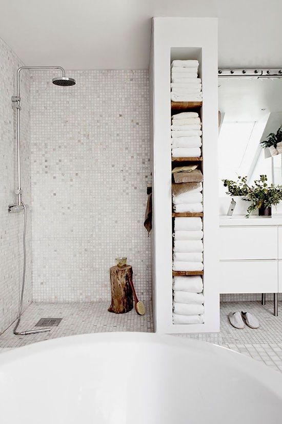 a white Scandinavian bathroom with small tiles, a tub, a pretty towel storage unit and a white vanity vanity
