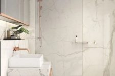 a white bathroom clad with marble, with large scale tiles, with a marble vanity and touches of copper here and there