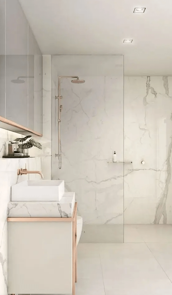a white bathroom clad with marble, with large scale tiles, with a marble vanity and touches of copper here and there