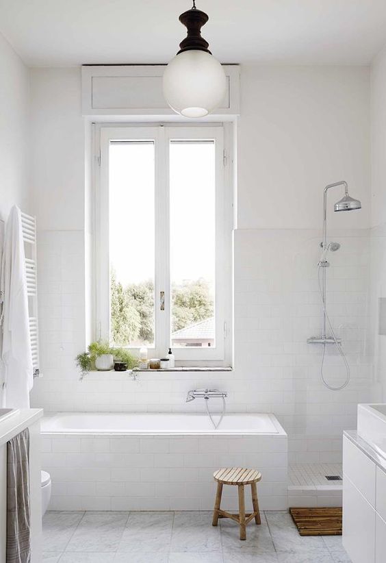 a white bathroom done with tiles, a tub, a shower, a white vanity, a radiator and some potted greenery, wooden touches