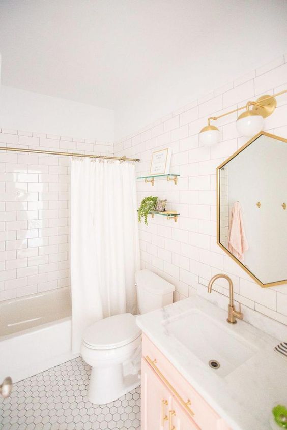 a white bathroom with a gold frame hexagon mirror, gold sconces, fixtures and a curtain rod