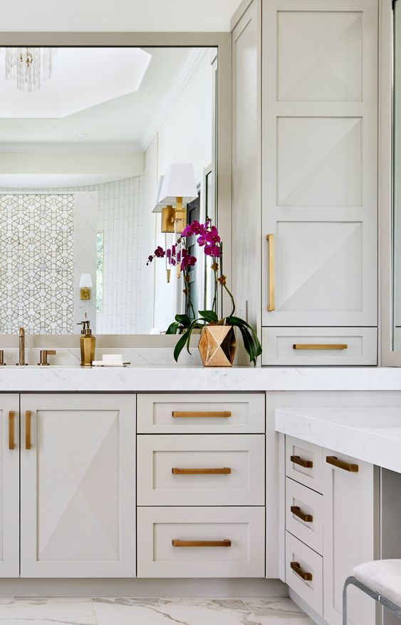 a white bathroom with an oversized vanity and storage units, gold and brass handles, gold fixtures and accessories