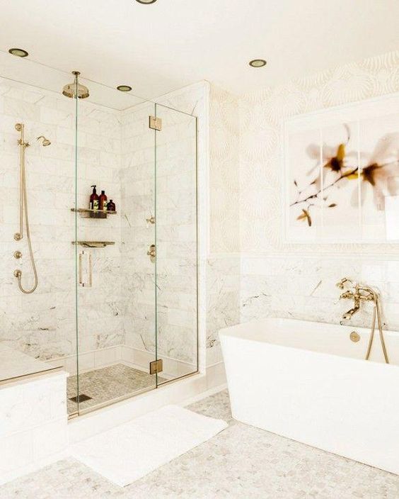 a white bathroom with different tiles, gold fixtures and sconces plus a pretty floral artwork