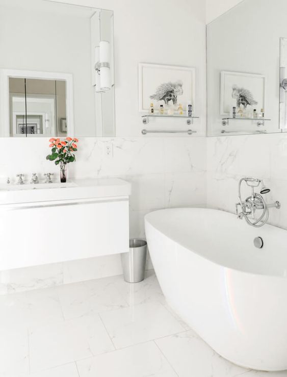 a white bathroom with large scale marble tiles, a tub, a floating vanity and a couple of mirrors