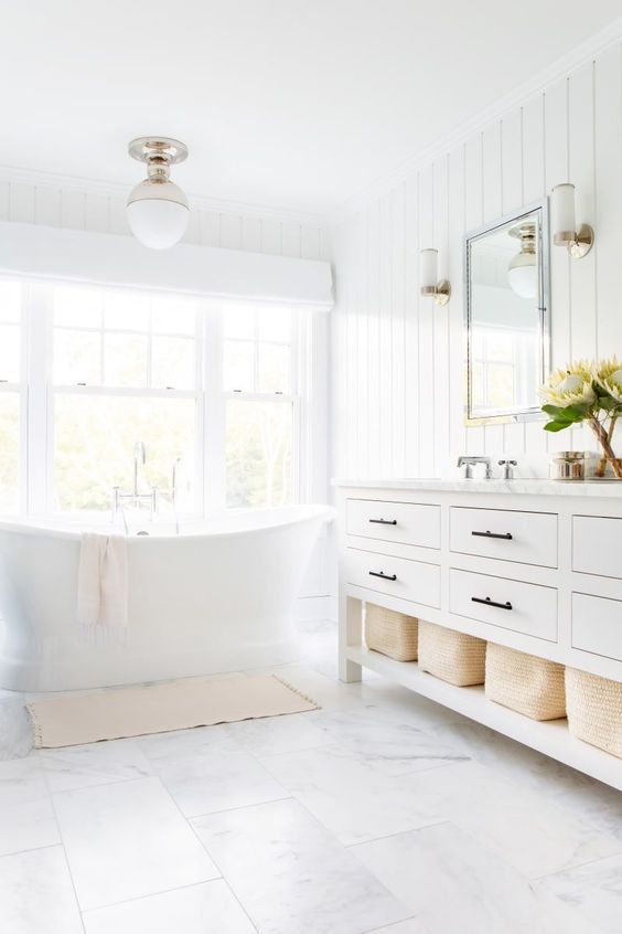 a white bathroom with shiplap walls, white marble tiles on the floor and a tub by the window looks very airy