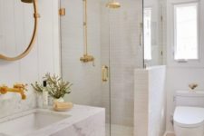 a white bathroom with various kinds of tiles, a floating marble vanity, gold and brass fixtures and sconces looks chic
