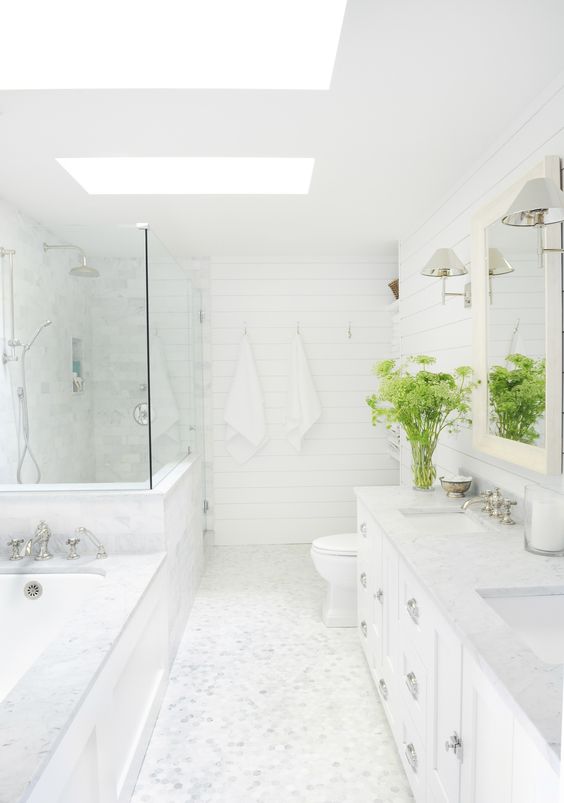 a white farmhouse bathroom with tiles, a shower space and a tub, skylights, a vanity, greenery and a mirror