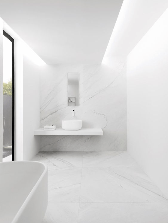 a white minimalist bathroom with a large window, a floating vanity, a bowl sink and a bathtub plus white marble