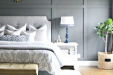an airy bedroom with a light grey paneled wall, upholstered furniture, printed textiles and rugs plus chic bold lamps