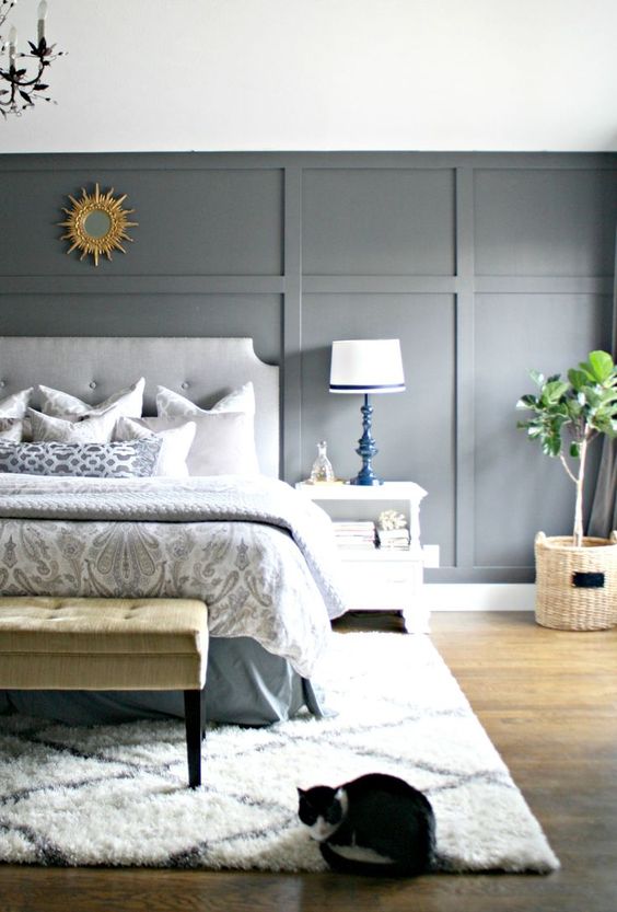 an airy bedroom with a light grey paneled wall, upholstered furniture, printed textiles and rugs plus chic bold lamps