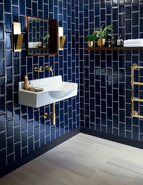 an elegant bathroom clad with navy tiles, spruced up with gold fixtures, lamps and accessories