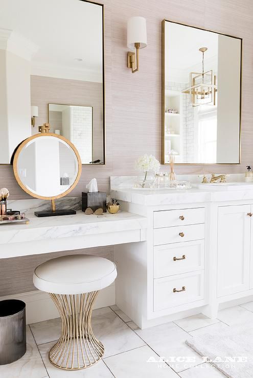 an elegant bathroom with a white vanity with a marble countertop, gold framed mirrors, a gold stool and sconces for accents
