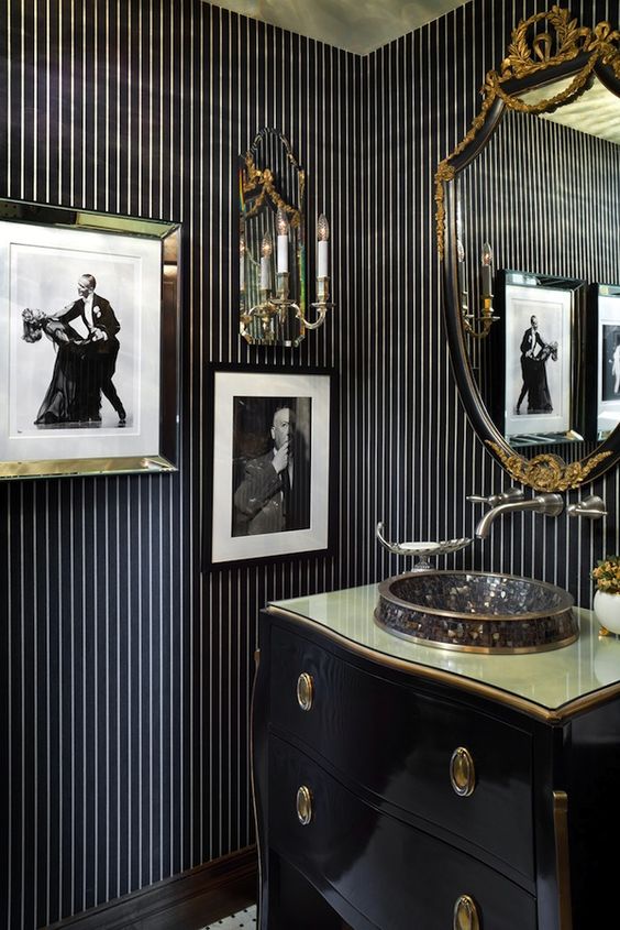 an elegant navy and gold bathroom with striped wallpaper walls, chic artworks and a catchy vintage vanity