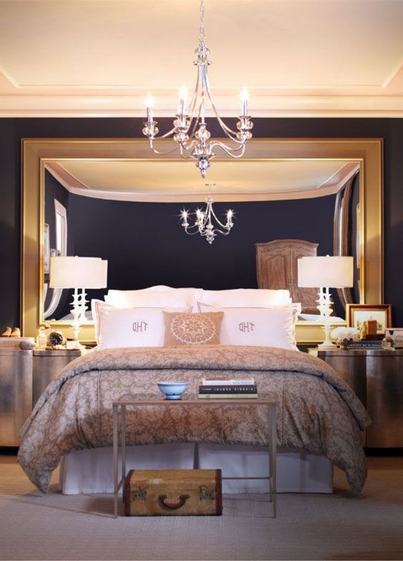 A chic modern bedroom with an oversized mirror in a gold frame, a chic chandelier and a couple of lamps for a refined feel
