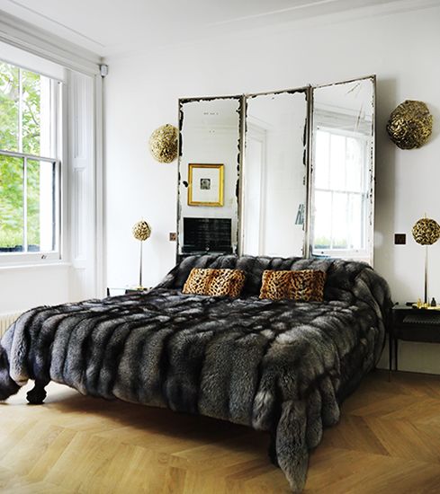 a modern luxurious bedroom with a vintage mirror as a headboard, a faux fur bedspread and some touches of gold