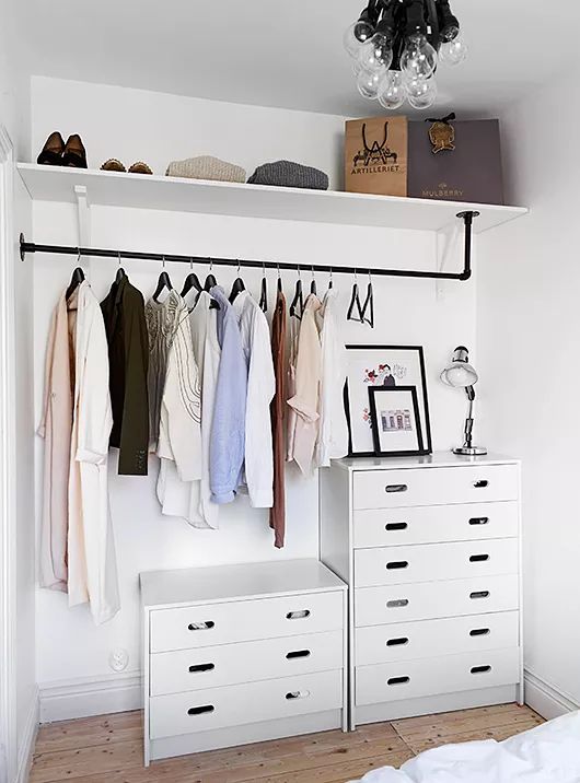 a small makeshift closet with dressers, a holder for hangers, an open shelf right in the bedroom