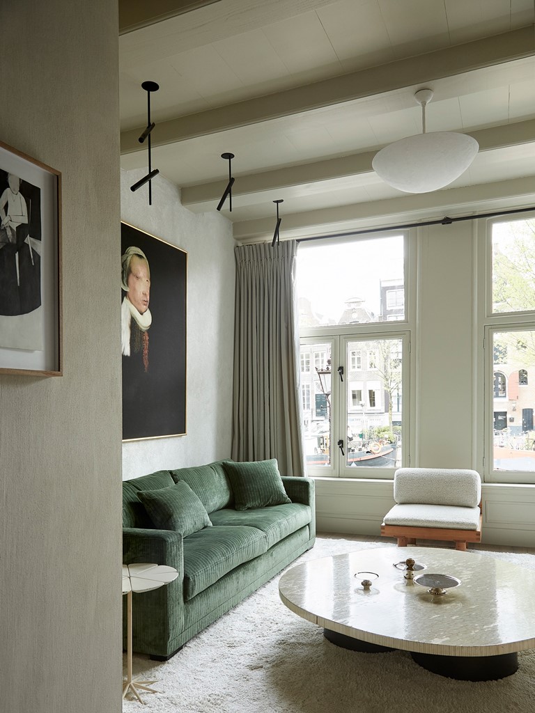 The living room is full of light, the furniture is neutral and muted colored, there are artworks