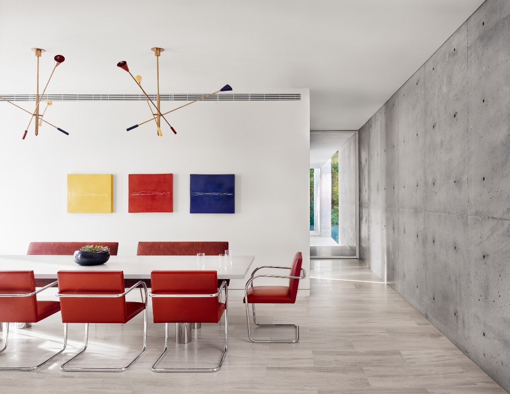 Bright red chairs and a colorful gallery wall spruce up the neutral dining room with a concrete accent wall