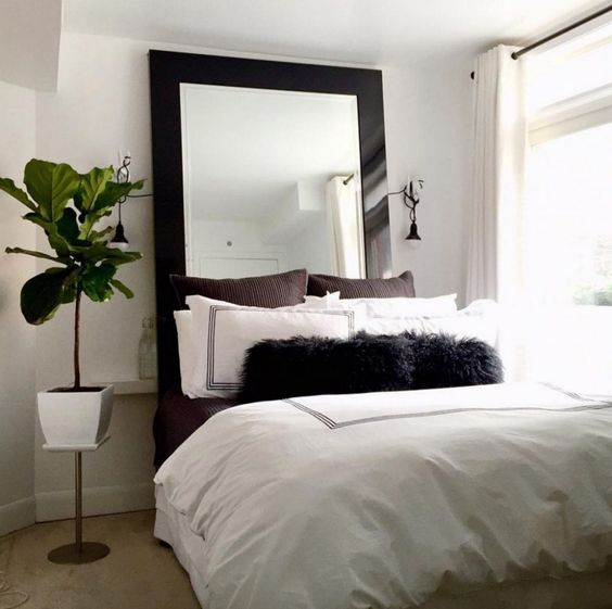 A small neutral bedroom with a modern statement mirror in a dark frame that catches an eye and makes the space cool