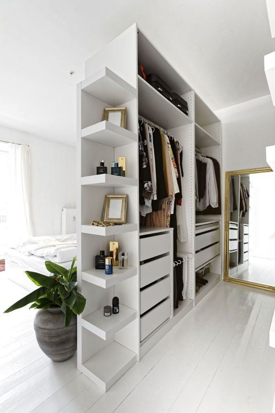 a small open closet in white with shelves, holders and drawers doubles as a space divider