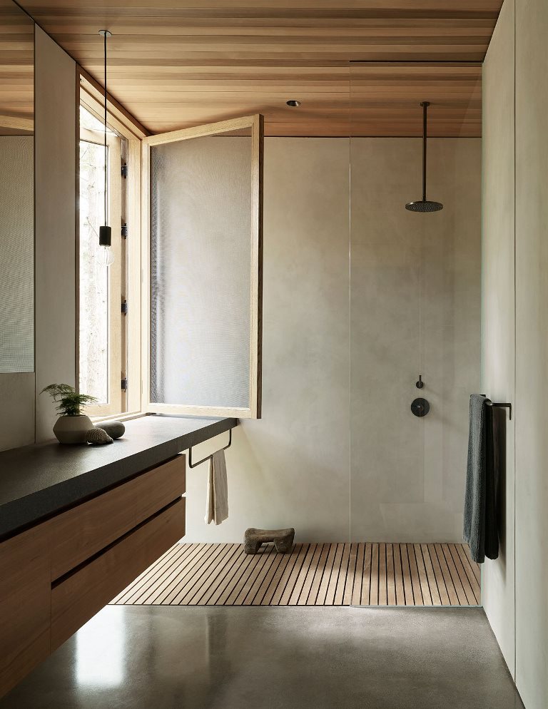 The bathroom is done with concrete and sleek wood, with dark fixtures and a window for a view