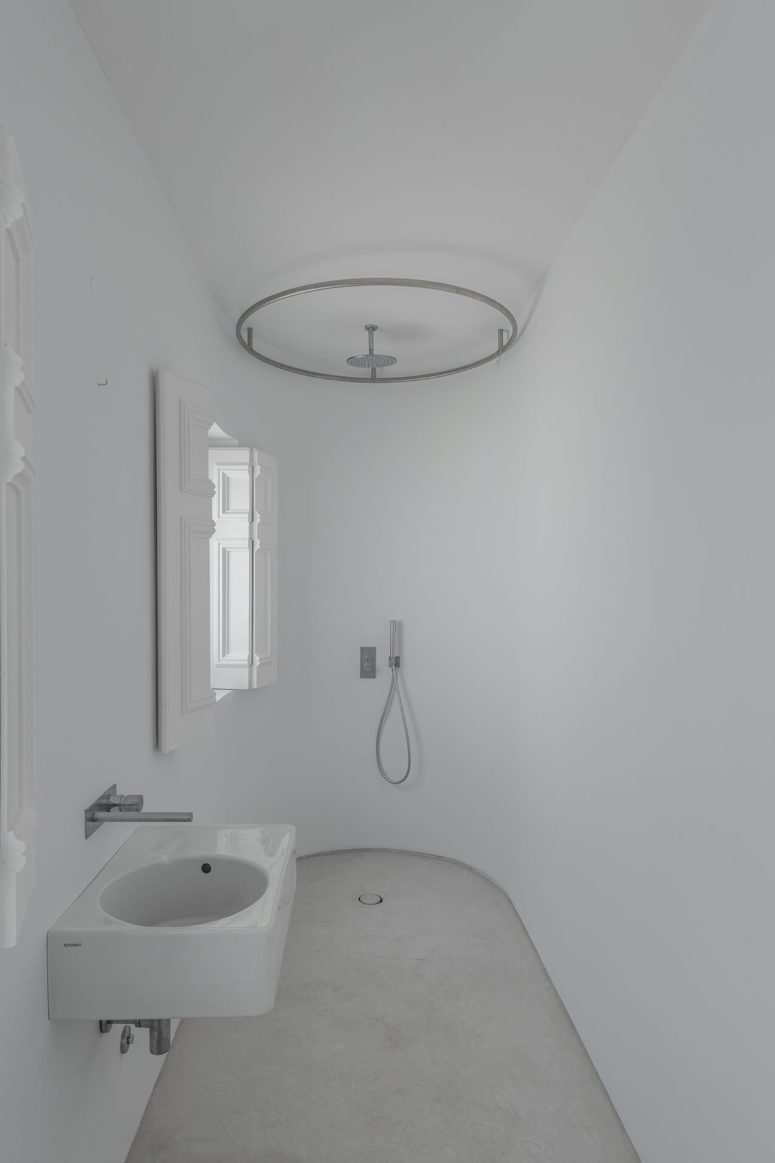 The bathroom is pure white, with a small shower space and a wall-mounted sink, the original shutters preserved